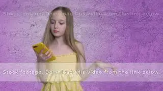 Blonde teen girl with long hairs is browsing smartphone on purple wall background.